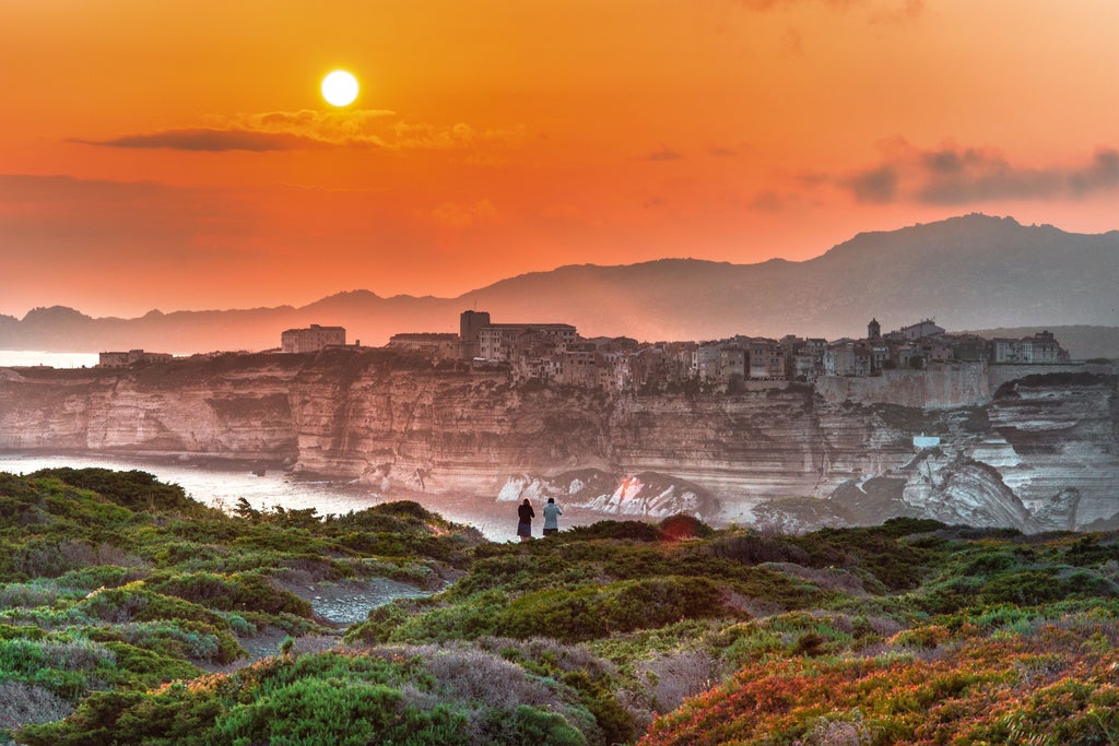 Crystal-clear Mediterranean waters meet rugged mountains along Corsica's coastline, with a luxury yacht anchored in a secluded turquoise bay