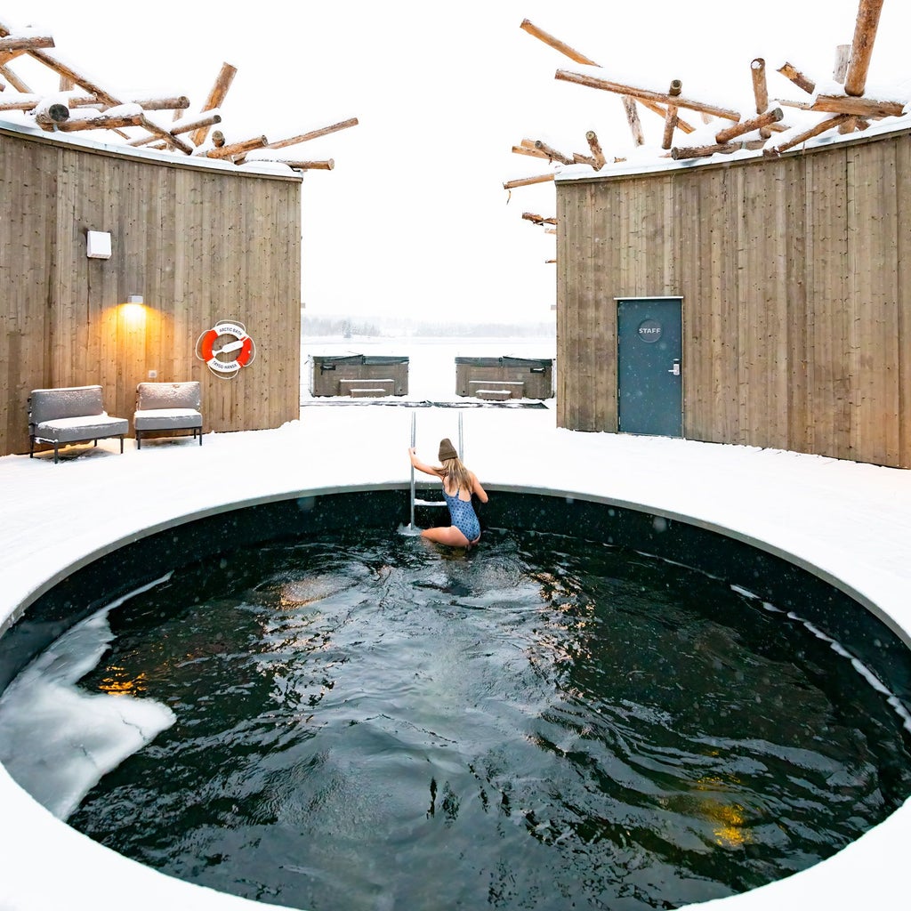 Luxurious circular wooden spa hotel suspended over frozen river in Arctic scenery, surrounded by snow-covered pine trees in Swedish Lapland