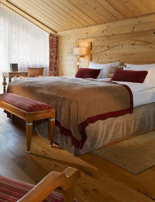 Luxurious alpine chalet suite with exposed wooden beams, plush furnishings, and mountain-view balcony at Mont Cervin Palace Hotel