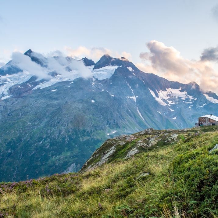 Luxurious Swiss alpine hotel with modern chalet-style architecture, snow-capped mountains, elegant wood and stone exterior at twilight with soft warm lighting