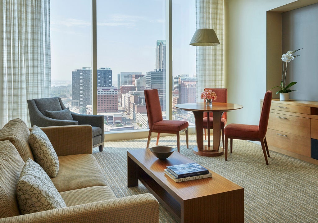 Modern luxury hotel tower with glass facade, rising above St. Louis skyline, featuring an illuminated rooftop infinity pool and river views