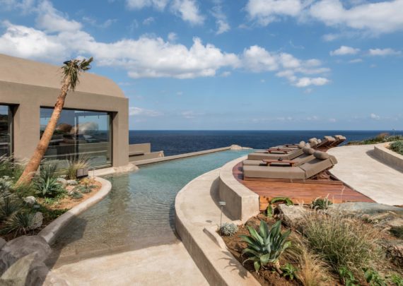 Elegant white stone hotel suite with private infinity pool overlooking the Aegean Sea and Santorini's volcanic caldera at sunset