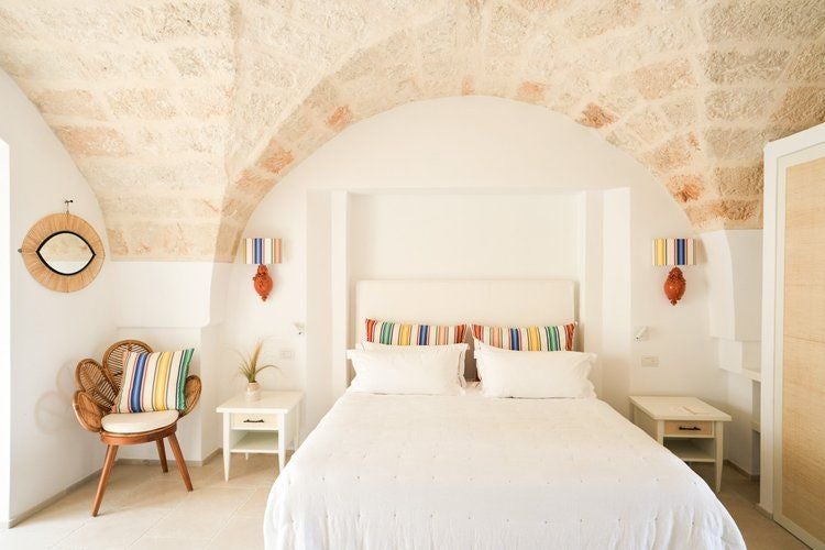 Rustic stone luxury room with arched window, crisp white linens, and warm terracotta tones overlooking scenic Puglia countryside at Masseria Calderisi