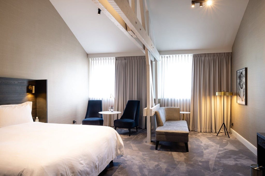 Elegant junior suite with plush white bedding, modern decor, soft ambient lighting, and sophisticated design in a luxurious Belgian boutique hotel room