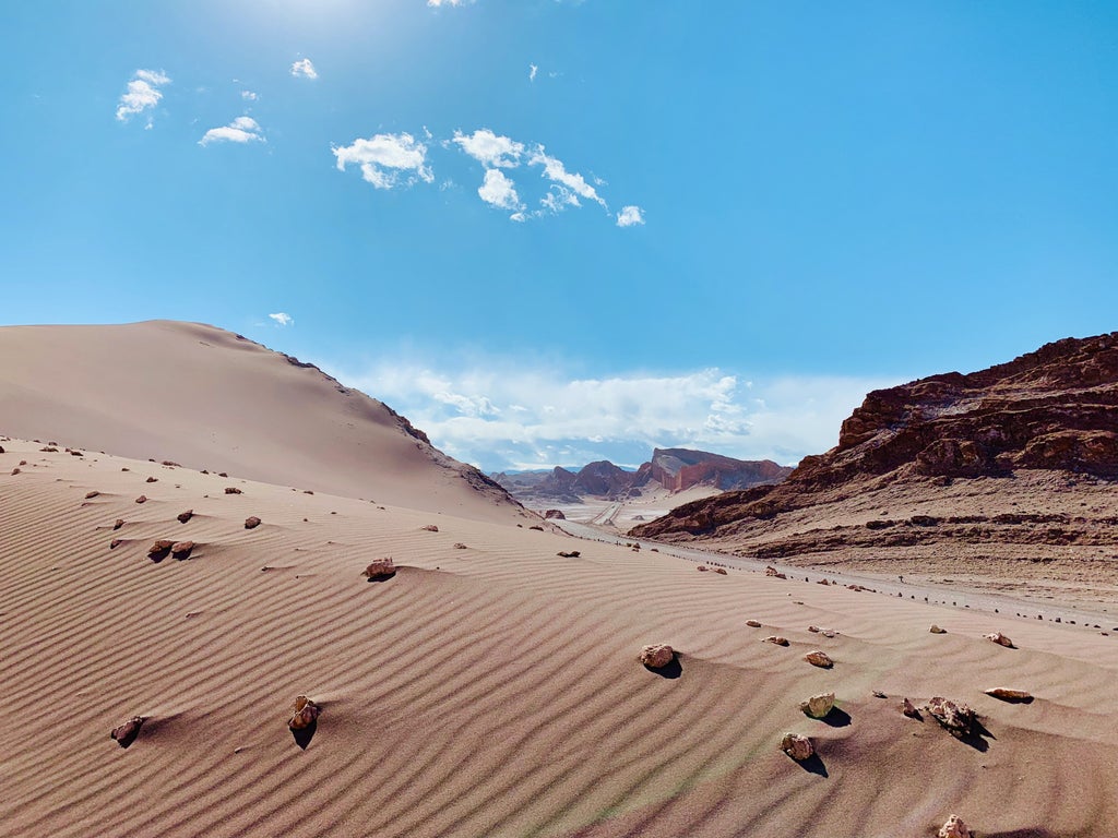 Pristine sand dunes stretch across Chile's Atacama Desert at sunset, with rugged Andes mountains silhouetted against an orange sky