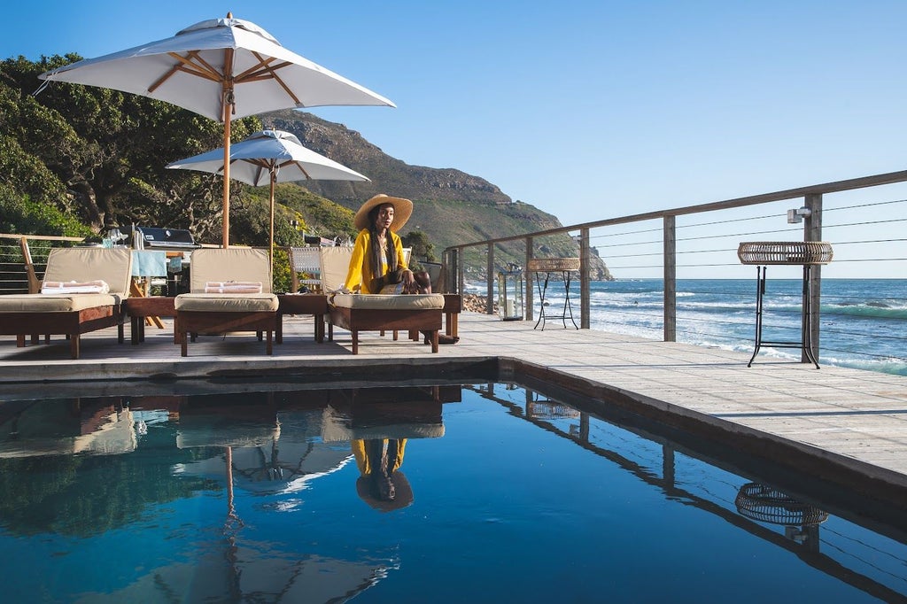 Luxury oceanfront lodge with infinity pool overlooking Chapman's Peak at sunset, nestled between mountain cliffs and Atlantic waves