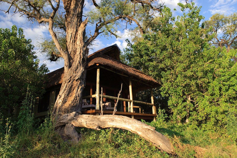 Elevated luxury safari tent overlooking African savanna at sunset, with private wooden deck and canvas roof against golden sky