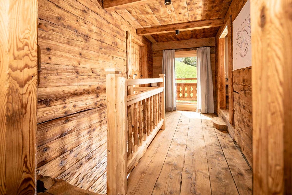 Traditional Austrian alpine hotel with wooden balconies, nestled against snow-capped mountains, surrounded by evergreen forest at sunset