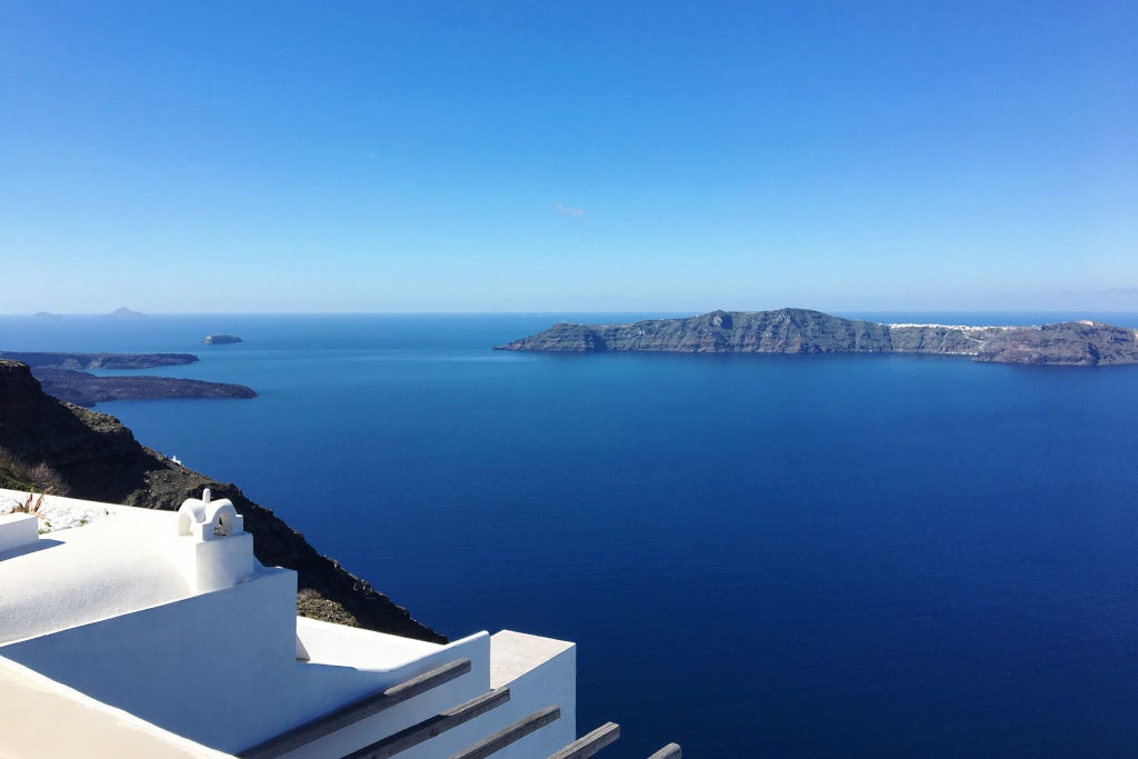 Luxurious white Cycladic suites with private pools overlooking the blue Aegean Sea and iconic Oia, Santorini sunset landscape at golden hour