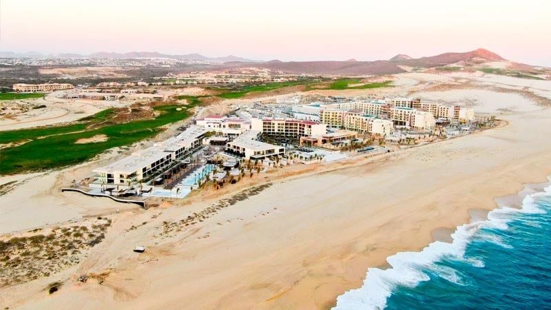 Sleek modern hotel buildings with infinity pools overlooking the Pacific Ocean, surrounded by desert landscaping and palm trees.