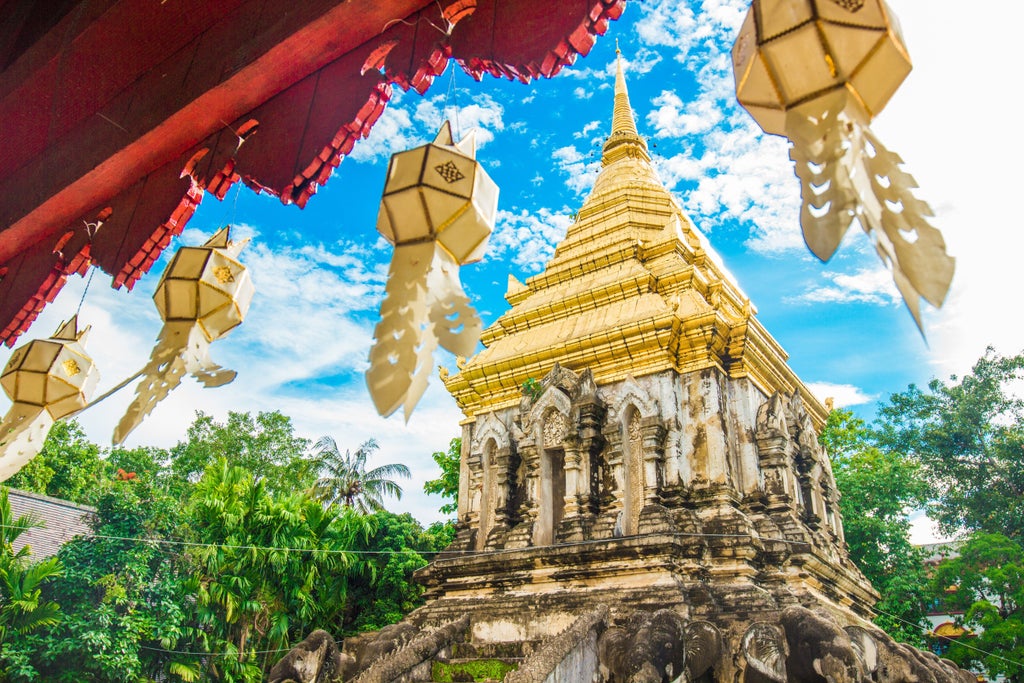 Ancient temple in Chiang Mai at sunset, with golden spires rising above lush gardens, ornate Thai architecture, and warm lighting casting long shadows