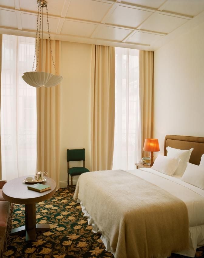 Elegant Parisian hotel room with plush king bed, rich burgundy walls, antique gold mirror, and soft ambient lighting at Château Voltaire