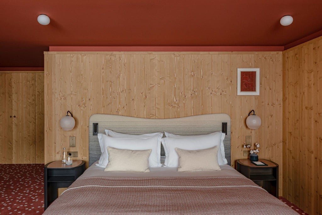 Luxurious alpine deluxe room at Le Coucou Méribel, featuring elegant wood-paneled walls, plush bedding, and stunning mountain view through large window