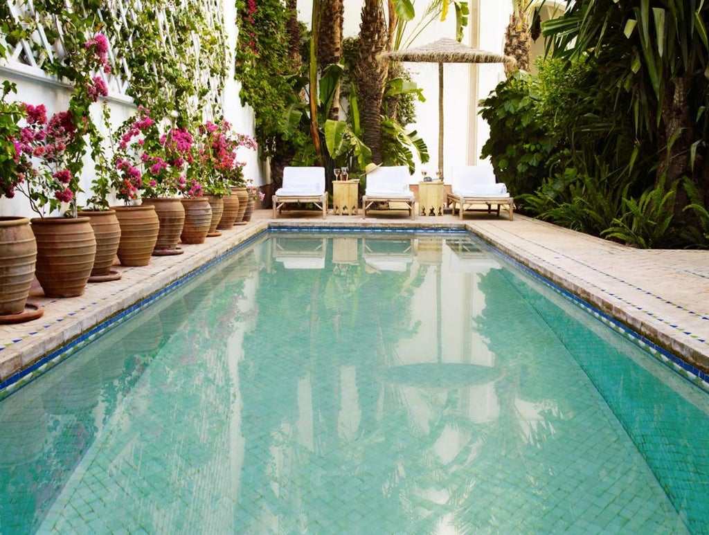 Grand courtyard of traditional Moroccan riad with ornate archways, white columns, emerald pool, and lush palms creating elegant symmetry