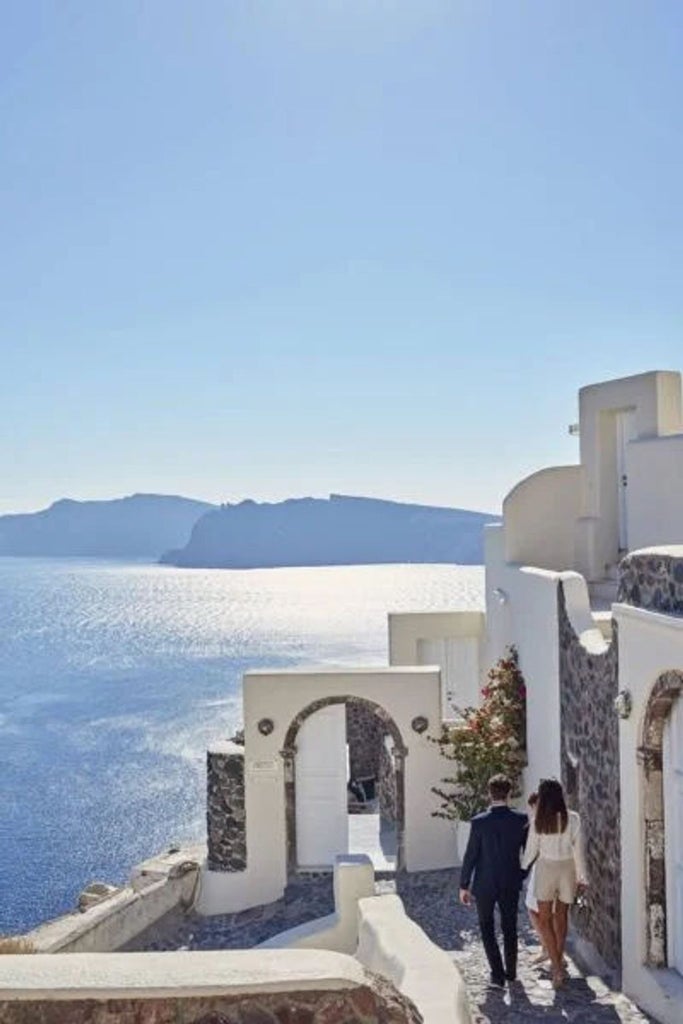 White luxury cave hotel suite with private infinity pool overlooking the blue Aegean Sea and Santorini caldera at sunset