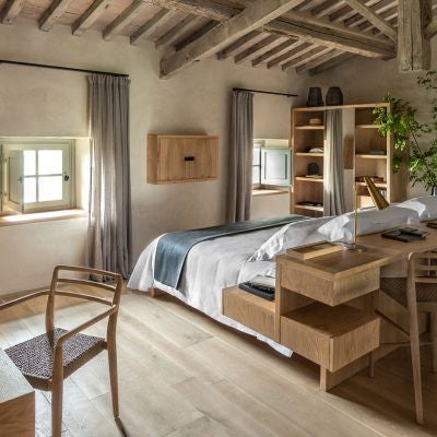 Elegant rustic Italian junior suite with exposed wooden beams, plush white bedding, and panoramic countryside view through arched window at Badia di Pomaio