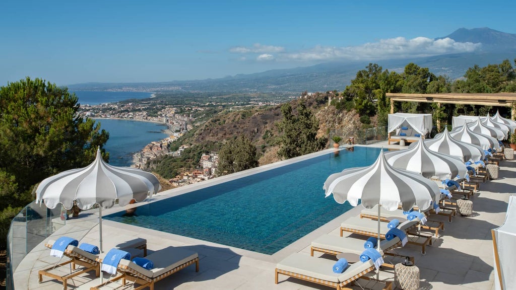 Elegant cliffside hotel overlooking Mediterranean Sea, featuring stone archways, manicured gardens and infinity pool at sunset in Sicily