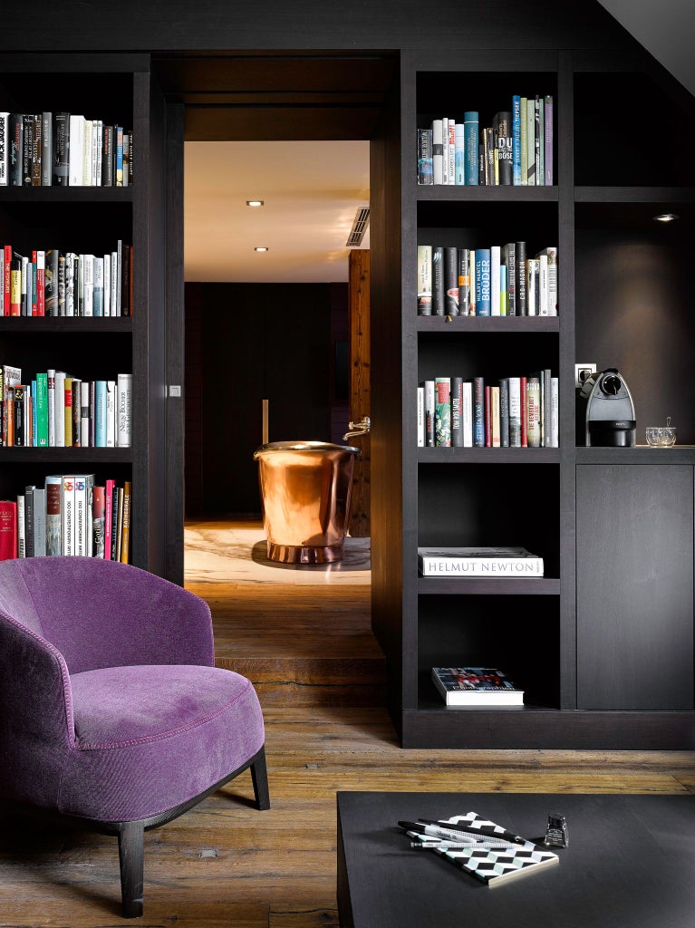 Elegant library suite with rich wooden bookshelves, luxurious leather armchair, warm ambient lighting, and classic European design in prestigious hotel room