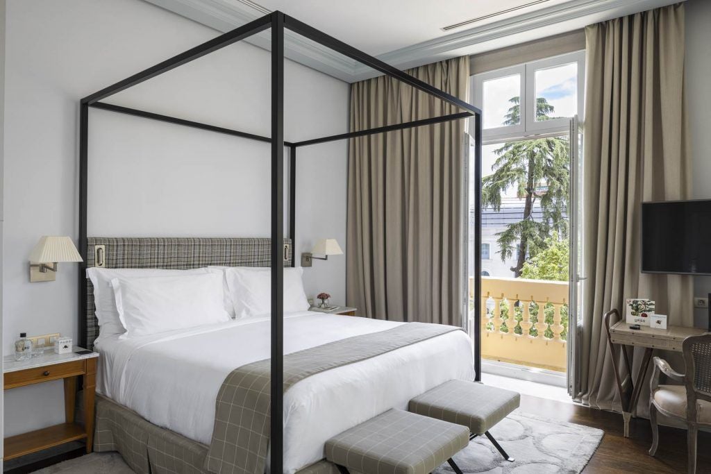 Elegant junior suite at URSO Hotel & Spa in Madrid, featuring plush white bedding, warm wood accents, and a spacious private terrace with city views