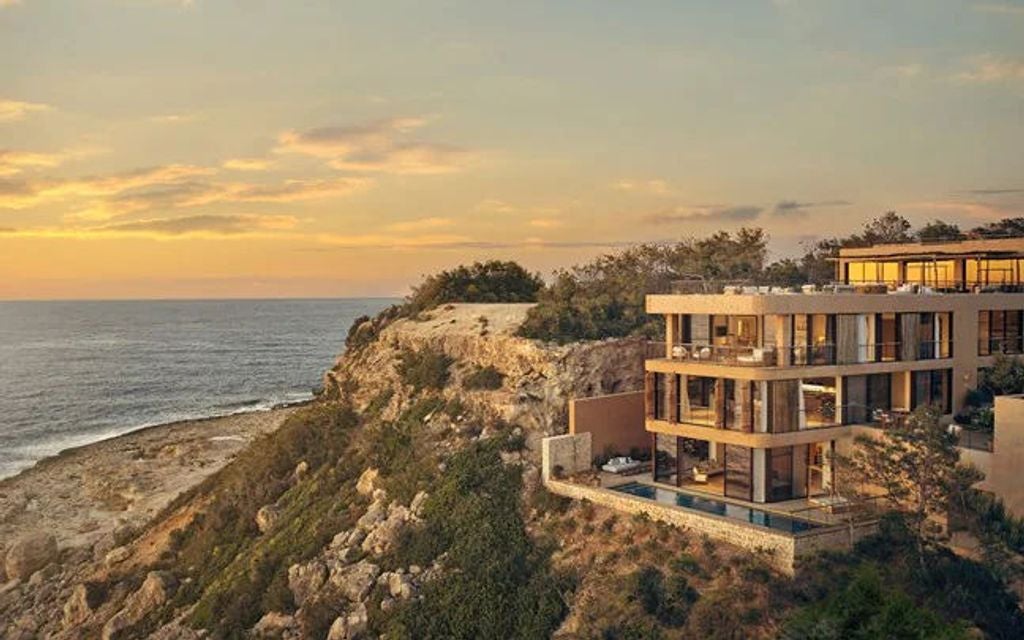 Minimalist white stone luxury resort with infinity pool overlooking Mediterranean Sea and Ibiza coastline at sunset, nestled in cliffside