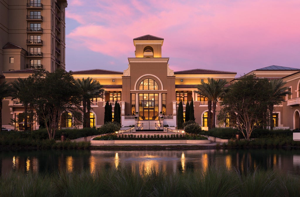 Modern lakeside luxury hotel with Spanish-style architecture, palm trees, and illuminated fountains at sunset in Walt Disney World Orlando