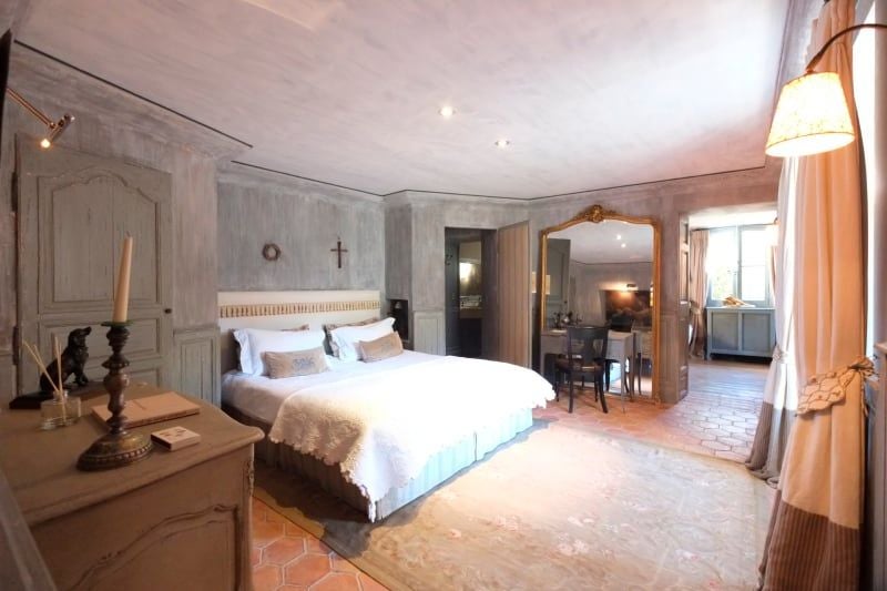 Elegant French luxury suite with soft rose-toned decor, plush white bedding, classic wooden furnishings, and large windows overlooking verdant landscape at Les Rosées