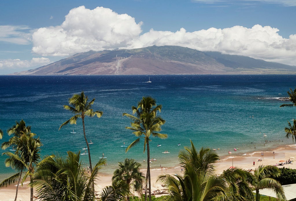 Luxurious oceanfront Hawaii resort with infinity pool overlooking Pacific, palm trees and cabanas against Maui's mountainous backdrop