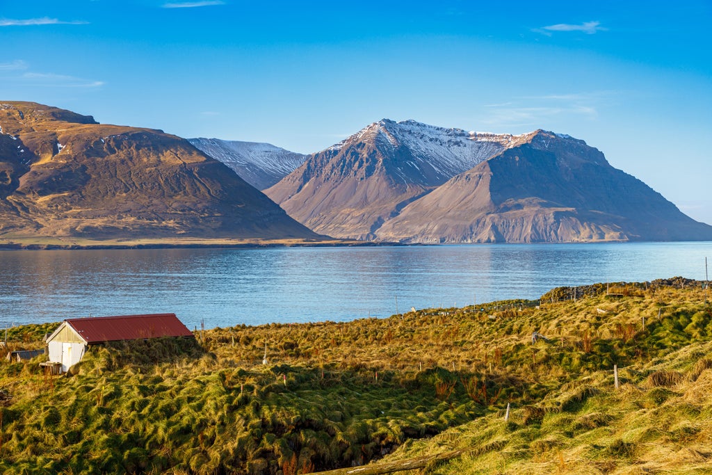 Dramatic Icelandic landscape with rugged cliffs, cascading Hraunfossar waterfall, and verdant moss-covered lava fields in Borgarfjörður's scenic wilderness