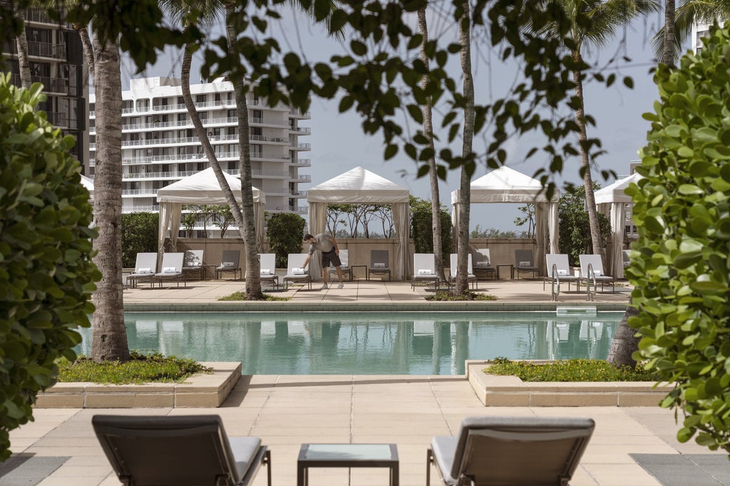 Elegant beachfront hotel with glass facade and palm-lined pool deck overlooking pristine Miami Beach waters at golden sunset