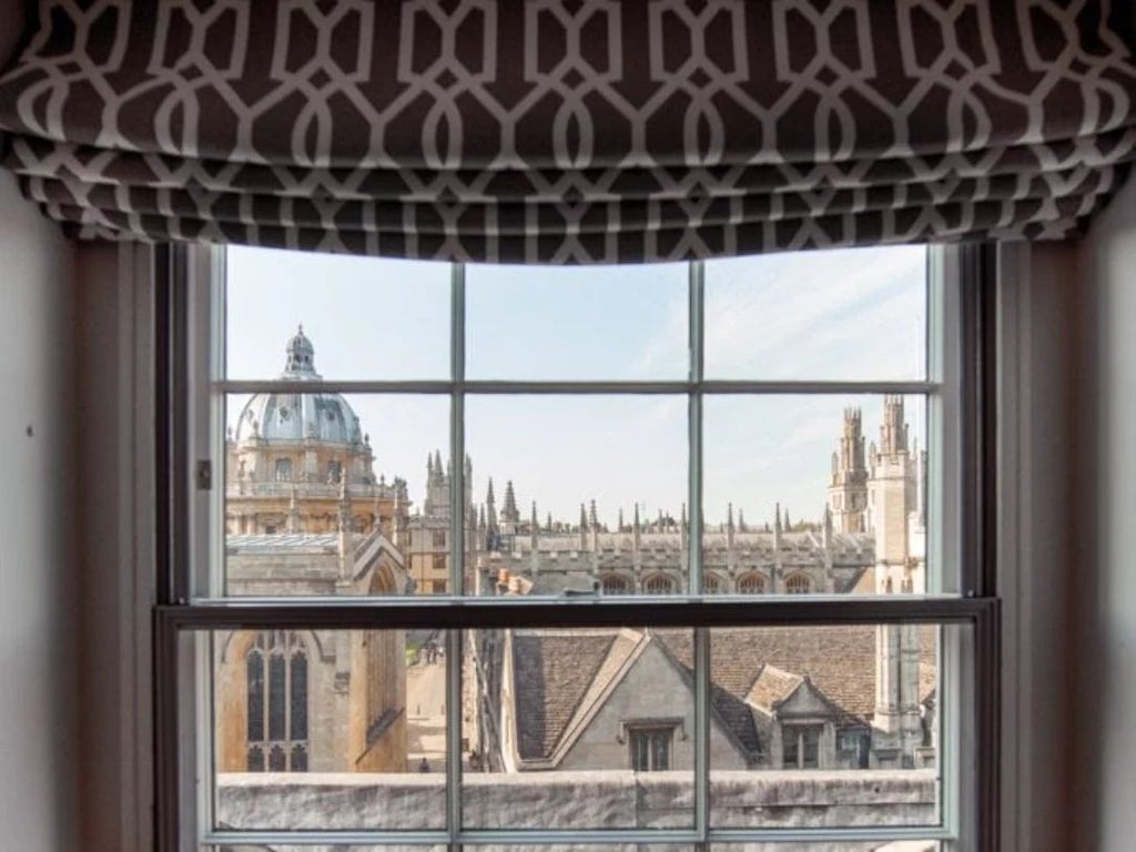 Elegant junior suite with period architectural details, rich mahogany furnishings, plush king bed, and large arched windows overlooking historic cityscape