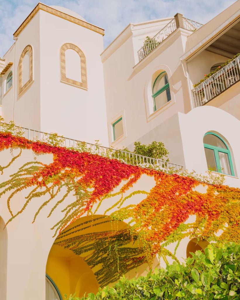 Historic Italian luxury hotel with infinity pool overlooking Amalfi Coast's dramatic cliffs and Mediterranean Sea at sunset