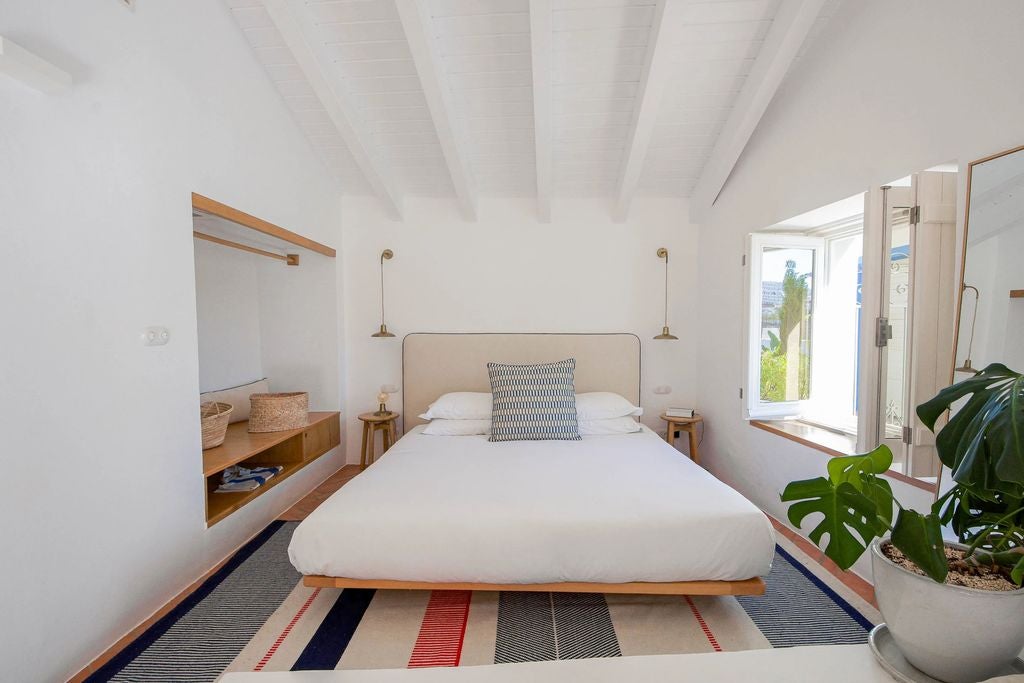 Bright sunlit boutique hotel room with rustic wooden desk, linen curtains, terracotta floor tiles and traditional Portuguese details