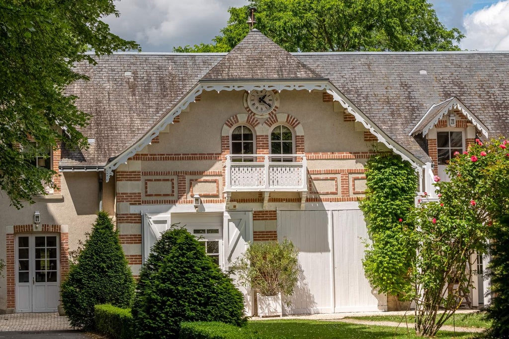 Historic French chateau with elegant cream facade, ornate windows, and manicured gardens surrounded by lush countryside at golden hour