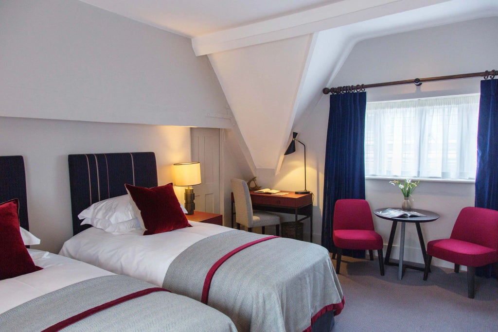 Elegant superior deluxe hotel room with refined decor, plush white bedding, warm wooden furnishings, and soft ambient lighting in a historic United Kingdom setting