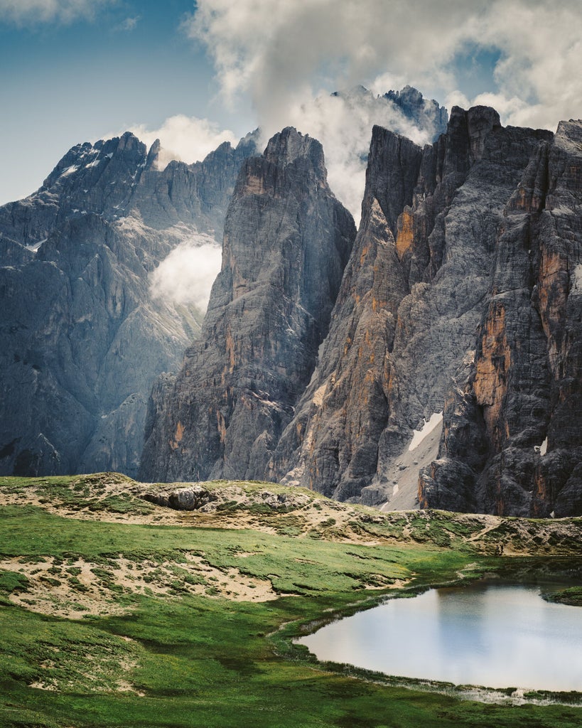 Majestic snow-capped Dolomite peaks rise above lush alpine meadows, with rustic chalets nestled beneath dramatic limestone cliffs at sunset