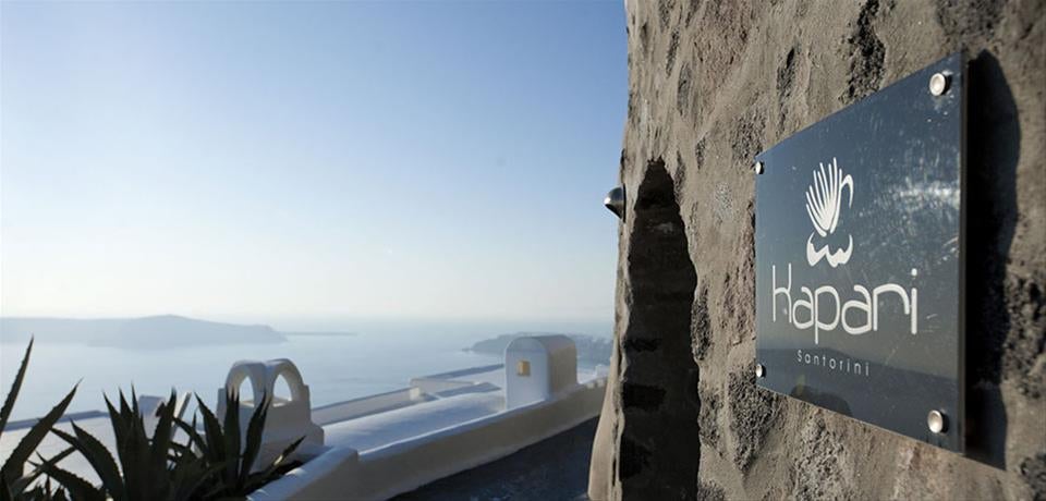 White-washed luxury cave hotel built into Santorini cliffs, featuring curved architecture and private infinity pools overlooking the Aegean Sea