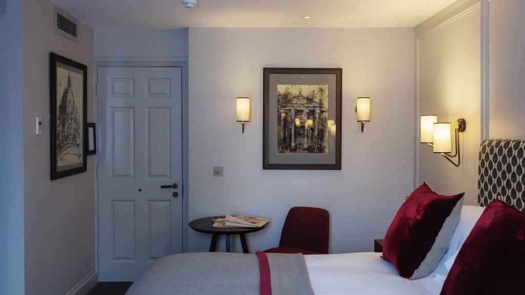 Elegant classic hotel room with plush white bedding, antique wooden furniture, soft neutral color palette, and large sash windows in a historic British setting