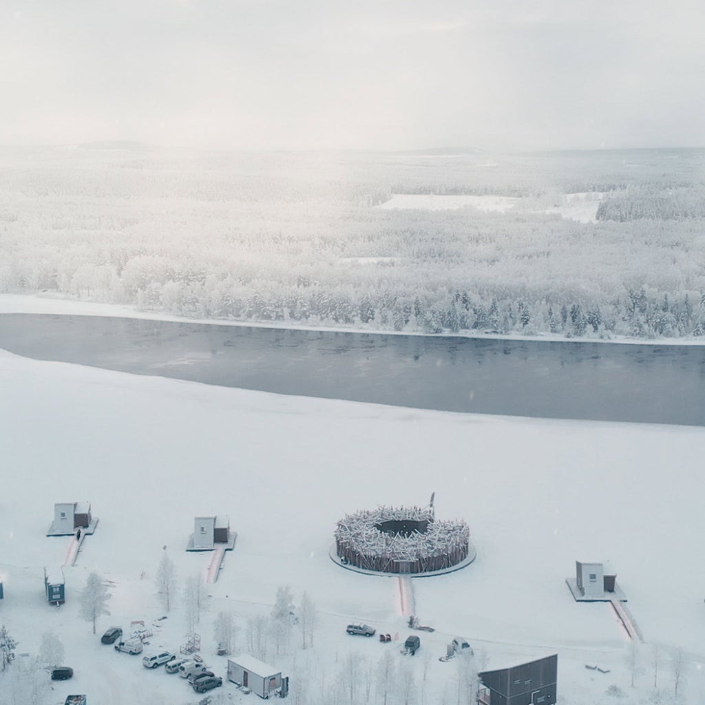 Floating circular wooden spa hotel nestled on frozen river, surrounded by snow-covered pine trees in Swedish Lapland's pristine winter landscape