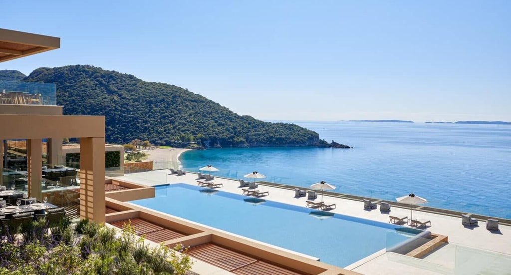 Elegant beachfront hotel with white modern architecture, infinity pool overlooking azure Ionian Sea waters in coastal landscape of scenic Greek destination