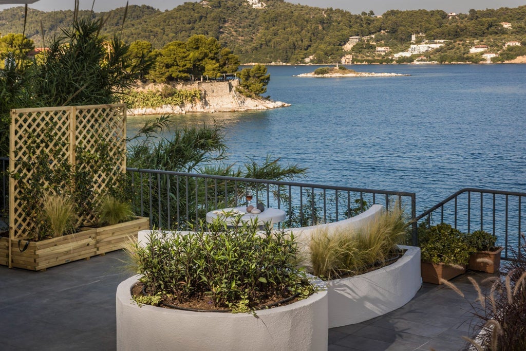 Elegant stone villa with terracotta roof overlooking azure Mediterranean waters, nestled in a lush Greek landscape with traditional architectural charm