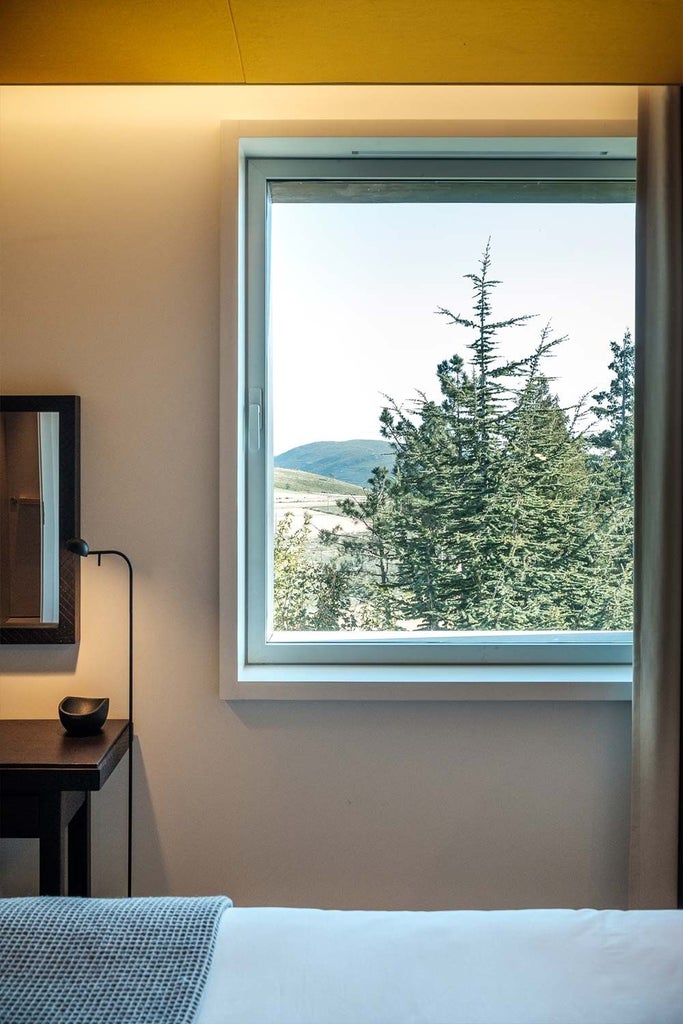 Elegant minimalist bedroom with white linens, warm wood tones, panoramic mountain view, and subtle Portuguese design elements by Maria Keil