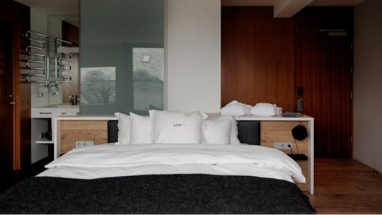 Sleek junior suite with minimalist Nordic design, panoramic city view, contemporary furnishings, and soft natural light in Icelandic urban hotel setting