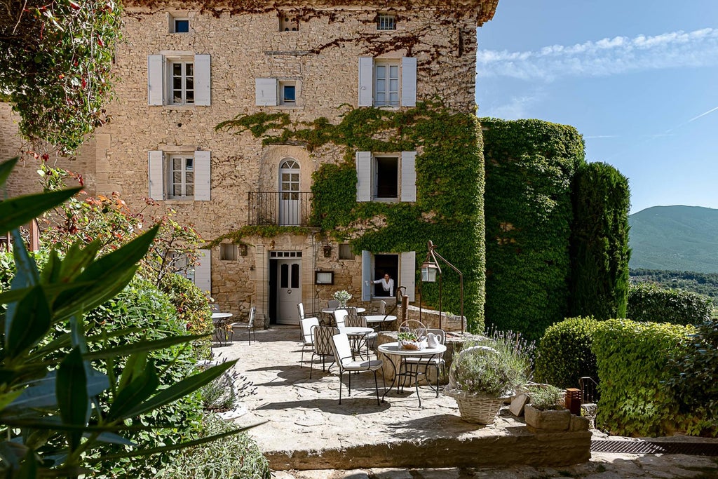 Elegant stone hotel nestled in French hillside with ivy-covered walls, terracotta rooftops, and panoramic views of Provence countryside