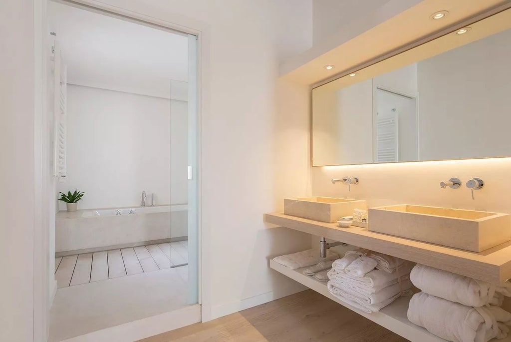 Elegant premium suite at Convent de la Missió, featuring sophisticated design with warm wooden floors, minimalist decor, and luxurious white bedding