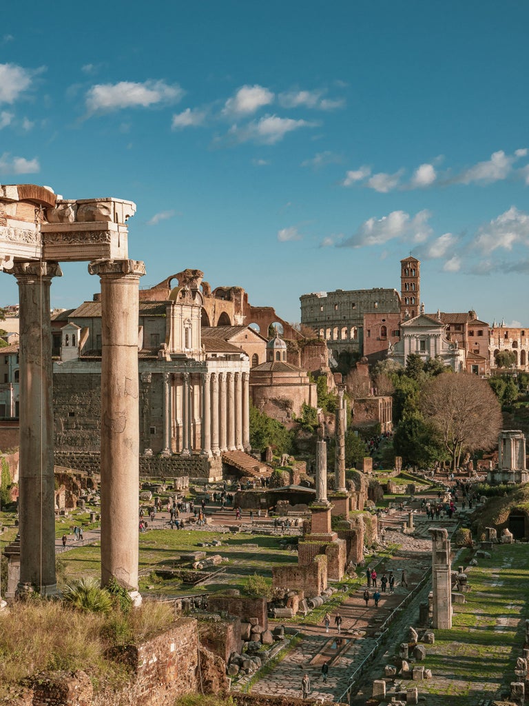 Ancient stone Colosseum in Rome at sunset, illuminated in warm golden light, with dramatic arched windows and classical architecture