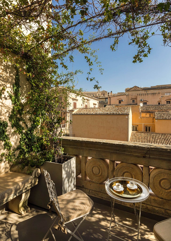 Elegant stone facade of historic Sicilian boutique hotel with wrought-iron balconies and warm limestone walls in Noto's baroque architectural style