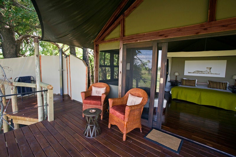 Elevated safari lodge suite with private deck overlooking Okavango Delta wetlands, featuring thatched roof and natural wood finishes