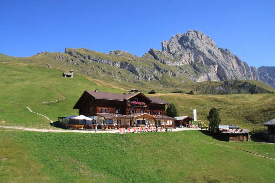 Mountain chalet with modern glass-walled restaurant perched on Dolomites cliffs, surrounded by snowy peaks and dramatic Alpine scenery