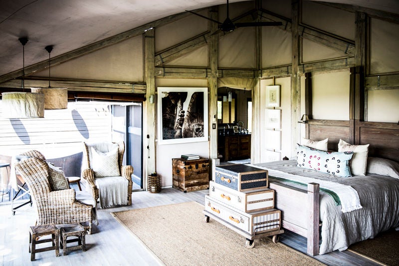 Safari lodge in Okavango Delta with private plunge pool overlooking savanna, thatched roof, and floor-to-ceiling glass doors at sunset