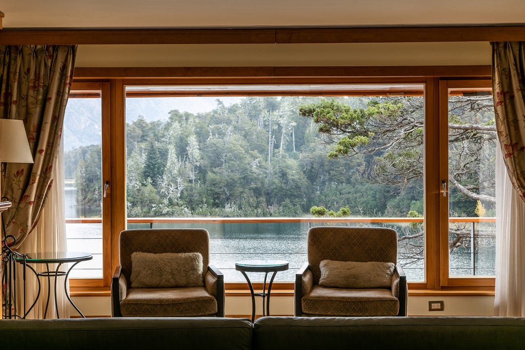 Mountain resort with alpine-style architecture nestled between snow-capped peaks and blue lake, featuring grand stone facade and manicured gardens